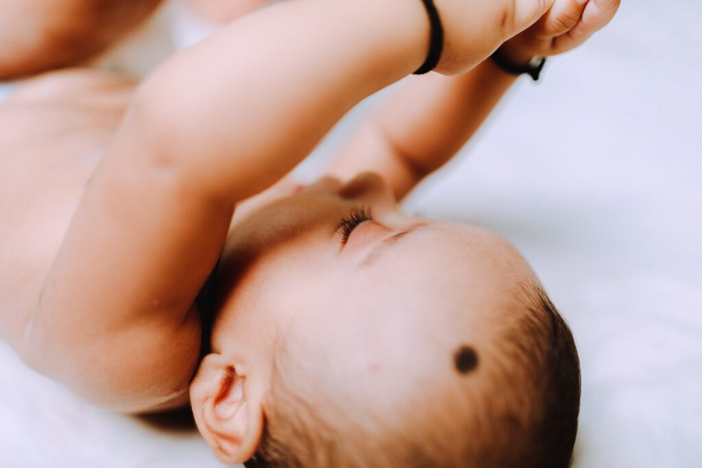 Baby lies on their back on a soft white surface, with their hands in the air. 